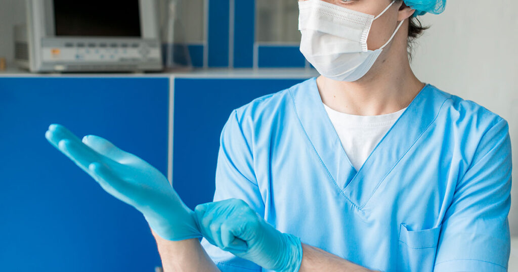 image of nurse with mask and hair covering on putting on gloves
