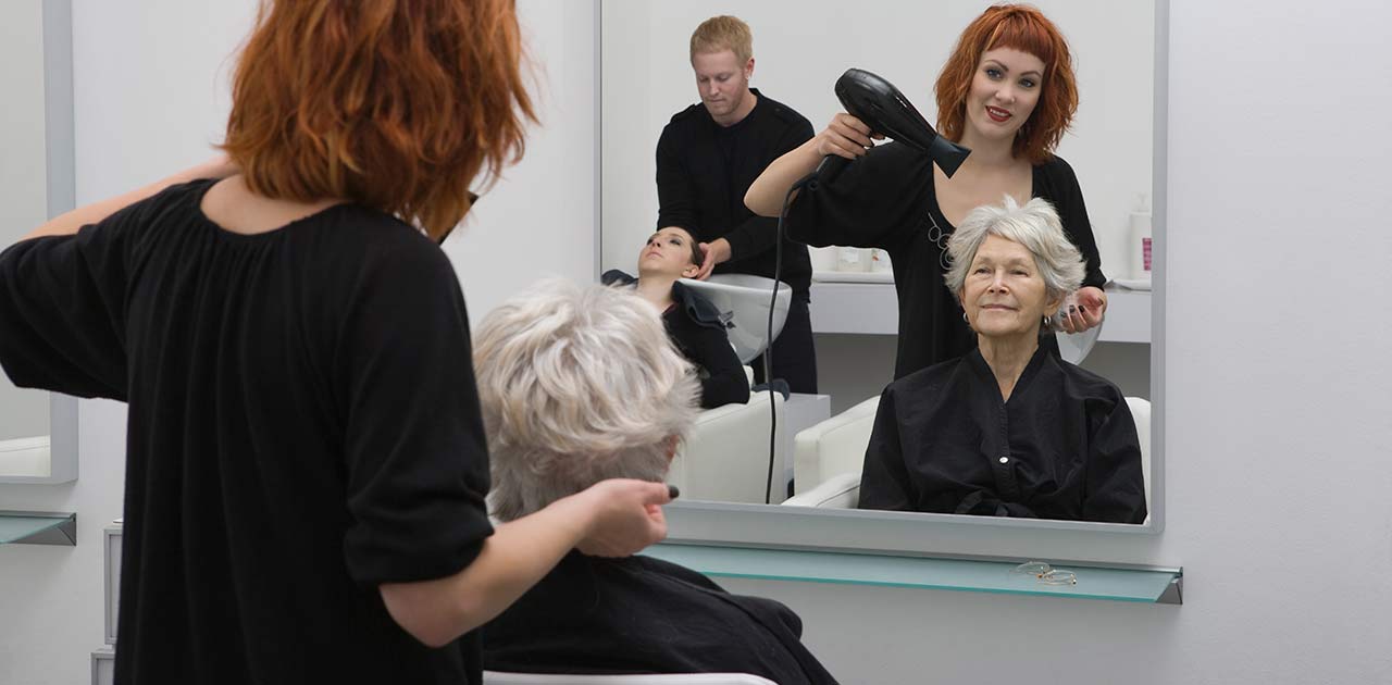 A hair stylist blow drying an older woman's hair